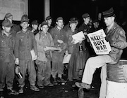 Pfc. Clarence K. Ayers of Evansville, Ind., reads the news of V-E Day as newly arrived German prisoners stand of a New York City pier, May 8, 1945.  (AP Photo/John Rooney)